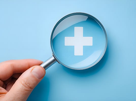 hand holding magnifying glass above a cross health sign